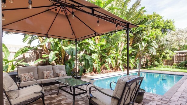 A poolside area with a covered seating area, a glass table, and a pool. - Poolside Boutique Guest House | Fort Lauderdale (Fort Lauderdale)