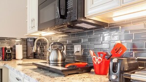 A kitchen with a stainless steel kettle, a toaster, and a red utensil holder on the counter. - Poolside Boutique Guest House | Fort Lauderdale (Fort Lauderdale)