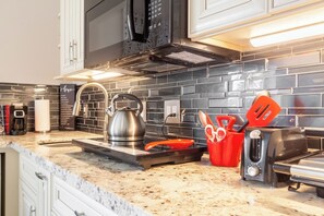 Una cocina con una tetera de acero inoxidable, un tostador y un recipiente rojo para utensilios en la encimera.