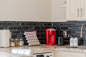 A kitchen with a black and white tiled backsplash, a red coffee maker, a toaster, and a jar of condiments.