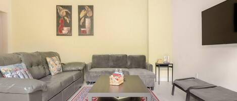 Una sala de estar con un sofá, una mesa de centro, un televisor montado en la pared y una alfombra estampada.