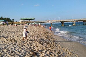Una playa con muelle, orilla arenosa y gente.