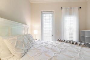 Un dormitorio con cama, mesita de noche, lámpara, puerta y ventana con persianas.