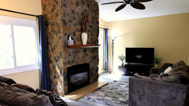 Una sala de estar con chimenea de piedra, un televisor de pantalla plana y un ventilador de techo.
