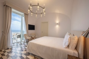 Quarto de hotel com cama, escrivaninha, cadeira, televisão e varanda com vista.