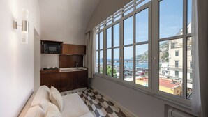 A room with a large window, a sofa, a kitchen area, and a view of the sea. - Bambagina Mare (Amalfi)