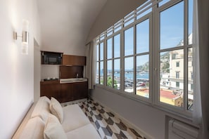 Quarto com uma janela grande, sofá, cozinha e vista para o mar.