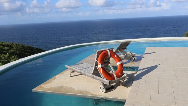 A pool with two lounge chairs and a lifebuoy, overlooking a body of water. - Jasdip, Aquatic Serenity where you can reset, relax, be free and breathe! (Cap Estate)