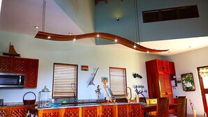 A spacious living area with a high ceiling, wooden beams, a large TV, and a dining area with wooden furniture. - Jasdip, Aquatic Serenity where you can reset, relax, be free and breathe! (Cap Estate)