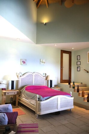 Une chambre à coucher comprenant un lit, des tables de chevet, une commode, un meuble à tiroirs, un miroir et un escalier.
