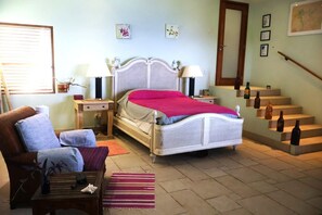 Une chambre à coucher comprenant un lit, des tables de chevet, une chaise, un canapé, un escalier et un mur orné de tableaux.