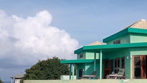 A green building with a covered outdoor area and lounge chairs. - Jasdip, Aquatic Serenity where you can reset, relax, be free and breathe! (Cap Estate)