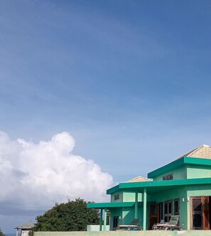 A green building with a covered outdoor area and lounge chairs.