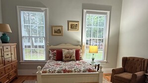 A bedroom with a bed, two windows, a ceiling fan, a chair, and a dresser.