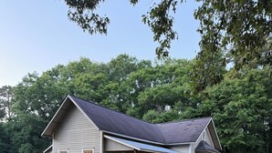 A single-story house with a porch, surrounded by a grassy yard and trees.