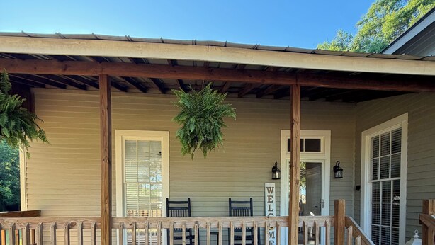 A wooden porch with a railing, a hanging plant, and a sign that reads 'WELCOME'.