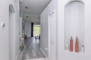 A hallway with a door, a chair, a table, and a window with a view. - Wesley Chapel Home 3Bed/2Bath with water view (Zephyrhills)