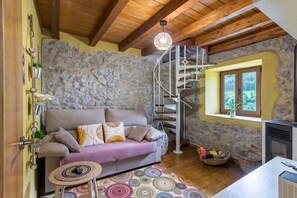 A cozy room with a stone wall, a wooden ceiling, a spiral staircase, a sofa, a small table, and a window with a view. - Vacation Home 'El Rincón De La Naturaleza' with Private Garden, Balcony and Wi-Fi (La Iglesia)