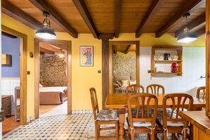Un comedor con sillas de madera y una mesa, una pared de piedra y una zona de cocina con estantes.