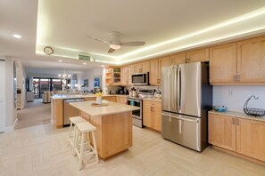 Eine moderne Küche mit Holzschränken, Edelstahlgeräten und einer zentralen Kochinsel mit Barhocker.
