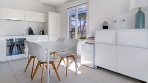 A modern kitchen with white cabinetry, a dining table with chairs, and a window with a view of the outside. - Cap Sud, Antibes – Quiet 2-Bedroom, Pool, Parking (Antibes)