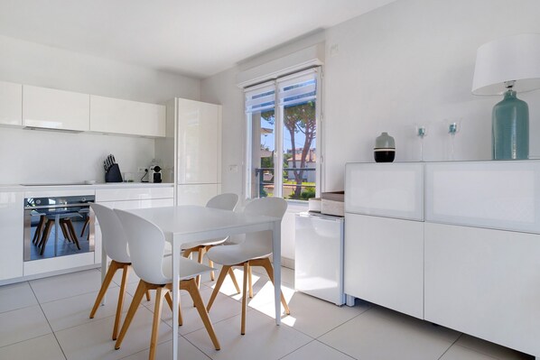 Une cuisine moderne avec des meubles blancs, une table à manger avec des chaises et une fenêtre donnant sur l’extérieur.