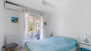 A bedroom with a bed, a chair, a desk, a ceiling fan, and a view through a window. - Cap Sud, Antibes – Quiet 2-Bedroom, Pool, Parking (Antibes)