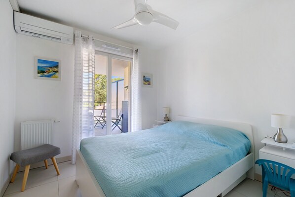Une chambre à coucher avec un lit, une chaise, un bureau, un ventilateur de plafond et une vue par la fenêtre.