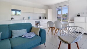A modern living space with a sofa, chairs, a dining table, and a kitchen area. - Cap Sud, Antibes – Quiet 2-Bedroom, Pool, Parking (Antibes)