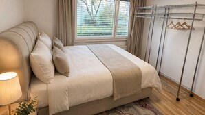 A bedroom with a bed, bedside lamp, window with curtains, and a hanging clothes rack. - Bern Garten Residence 152m Luxury Apartment (Bern)