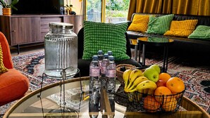 A living room with a sofa, a coffee table with fruit and water bottles, a TV, and a window with curtains. - Bern Garten Residence 152m Luxury Apartment (Bern)