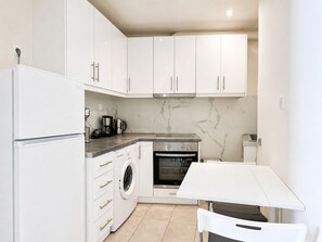 Eine kleine Küche mit weißen Schränken, einem Backofen, einer Waschmaschine und einer Kaffeemaschine.
