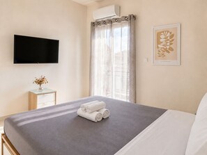 Ein Hotelzimmer mit Bett, Flachbildfernseher, einem kleinen Tisch mit einer Vase und einem Fenster mit Vorhängen.