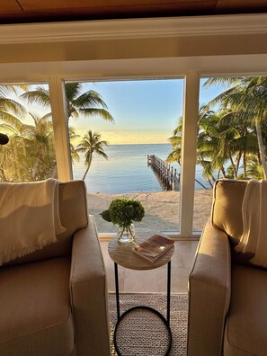 A room with a view of a beach, two sofas, a small table with a plant, and a wooden deck extending into the water. - Southwind Private Beachfront Estate with Infinity Pool, Spa and Fishing Pier (Islamorada)