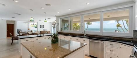 A spacious kitchen with a large island, white cabinetry, and a view of the ocean.