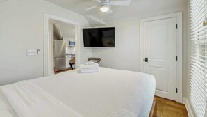 Ein Schlafzimmer mit Bett, Deckenventilator, Fernseher, Tür und Schrank.