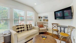 Ein Wohnzimmer mit Sofa, Sessel, Couchtisch, Fernseher und einem kleinen Tisch mit Stühlen.