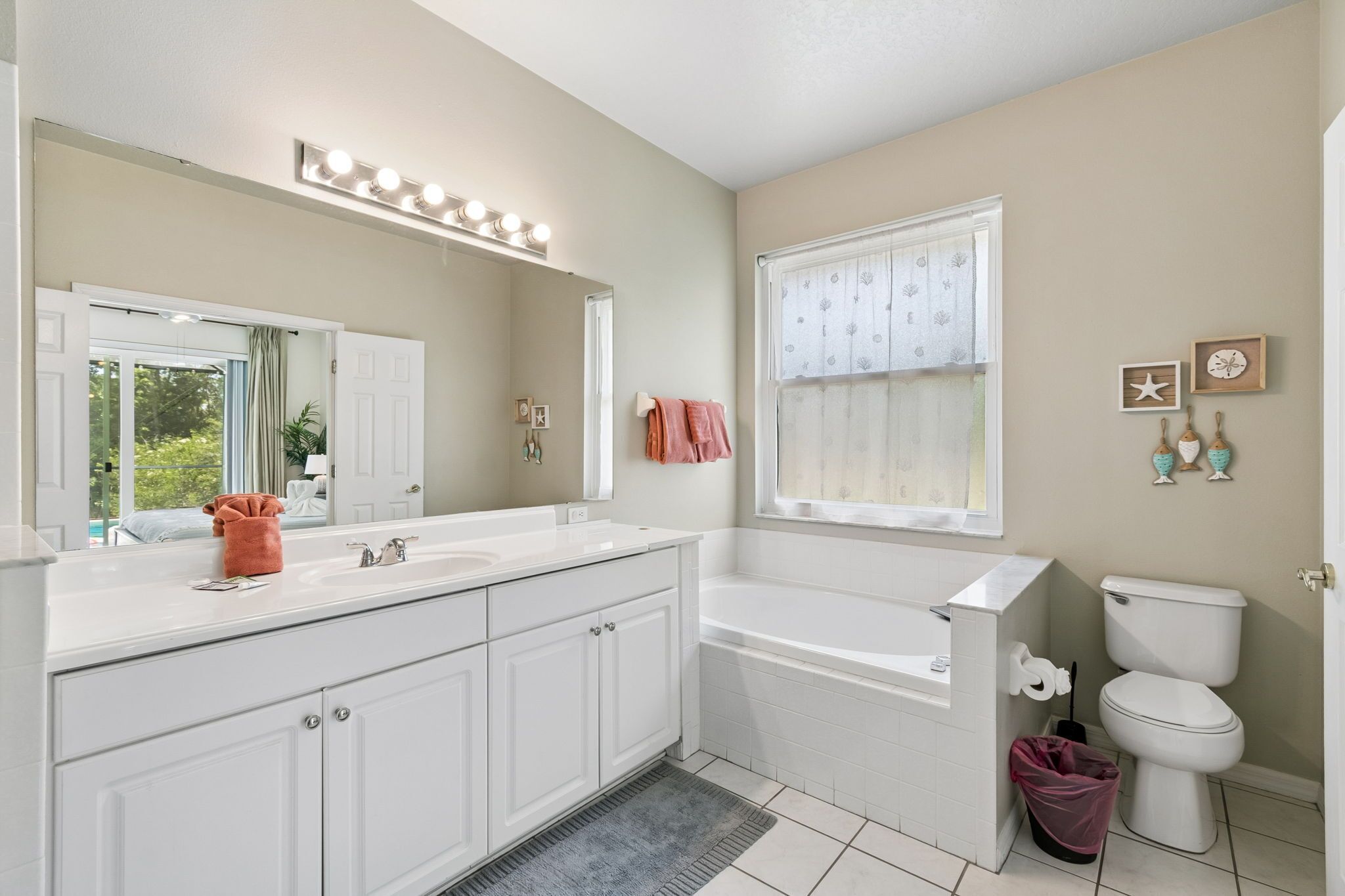 A bathroom with a large mirror, vanity, bathtub, toilet, and a window with curtains.