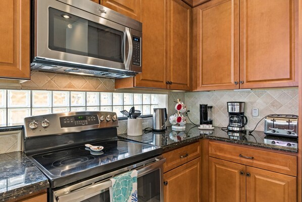 Una cocina con electrodomésticos de acero inoxidable, armarios de madera, salpicadero de azulejos y una encimera con diversos objetos.