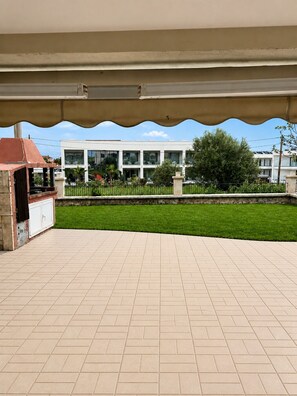 Ein überdachter Patio-Bereich mit Grill und Blick auf ein Gebäude mit zahlreichen Fenstern.