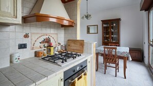 A kitchen with a gas stove, oven, and a dining area with a table and chairs. - Relaxation near Rome with bright terrace, perfect for 2-4 guests (Roma)