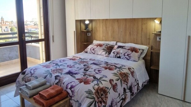 A bedroom with a bed, a bench with towels, a wooden headboard, and a view through a large window. - Relaxation near Rome with bright terrace, perfect for 2-4 guests (Roma)
