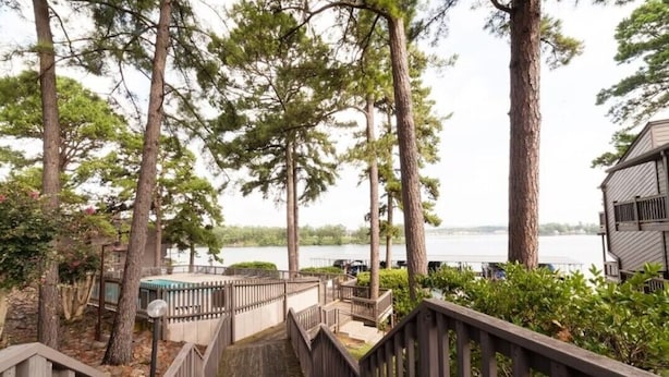 Una scala in legno conduce a un terrazzo con vista su un lago, circondato da alberi alti.