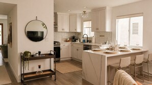 Una cocina moderna con armarios blancos, una isla central con asientos, un espejo redondo y una lámpara colgante.