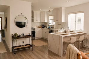A modern kitchen with white cabinets, a central island with seating, a round mirror, and a hanging light fixture. - Chic Designer Home, Walkable to Marine Stadium and Minutes to Beach & 2nd Street (Long Beach)