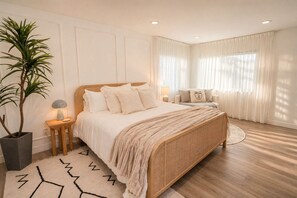 A bedroom with a large bed, bedside tables, a potted plant, and a window with curtains. - Chic Designer Home, Walkable to Marine Stadium and Minutes to Beach & 2nd Street (Long Beach)