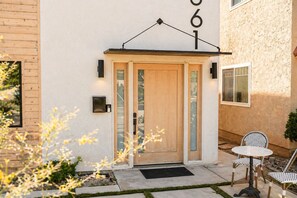 A modern building entrance with a wooden door, a number sign, and outdoor seating. - Chic Designer Home, Walkable to Marine Stadium and Minutes to Beach & 2nd Street (Long Beach)