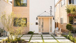 Una casa moderna de dos pisos con fachada de madera, una puerta central con paneles de vidrio y el número '361' en la parte superior.