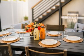 A dining table set with plates, glasses, and two bottles of orange juice. - Chic Designer Home, Walkable to Marine Stadium and Minutes to Beach & 2nd Street (Long Beach)