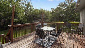 A wooden deck with a table and chairs, surrounded by a wooden railing and trees. - Family Favorite_Sleeps 8_Roomy_Game Room (Lenexa)